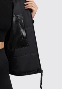 Interior de chaqueta de plumas negra con un bolsillo con cremallera negra brillante. La tela es suave, y la textura parece blanda y acolchada.