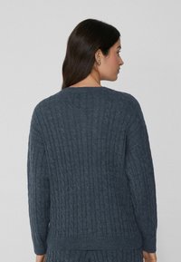 Sweter w sploty kablowe w ciemnoszarym kolorze, z prążkowaną teksturą, długimi rękawami i okrągłym dekoltem. Tył prezentuje pionowe wzory.