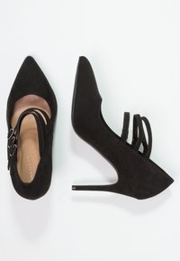 Svarta mocka högklackade skor med spetsig tå och utskärningsdesign, med flera smala remmar och en smal stiletto-klack.