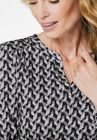 Schwarz-weiße Bluse mit geometrischem Muster, V-Ausschnitt und weichem Stoff. Leichte Raffungen an den Schultern.