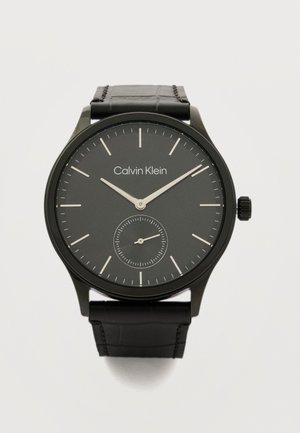Schwarze Calvin Klein Armbanduhr mit Lederarmband, minimalistischem Zifferblatt, silbernen Zeigern und kleiner Sekundenanzeige bei sechs Uhr.