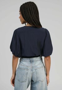 Blouse marine à manches courtes avec des épaules bouffantes et un décolleté arrondi, assortie à un jean en denim bleu clair taille haute.