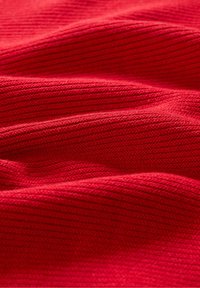 Tissu tricoté rouge avec une texture côtelée, affichant de douces vagues et des nuances de couleur variées, indiquant profondeur et richesse.