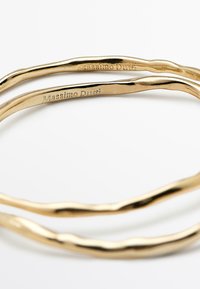 Due braccialetti intrecciati color oro con un design attorcigliato, caratterizzati da una texture liscia e dal nome del marchio inciso, Massimo Dutti.