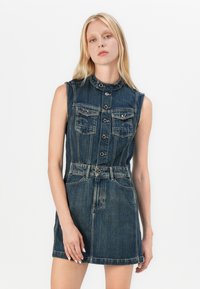 Denim dress with sleeveless design, dark blue color, button front, two chest pockets, a fitted waist, and a flared skirt.
