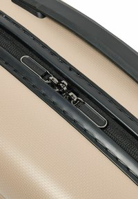 Close-up van een beige gestructureerde koffer met een zwarte rits en dubbele metalen ritstrekkers die zijn gegraveerd met "REDOLZ."