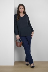 Mörk marinblå långärmad topp med V-ringning, kombinerad med smala blå jeans. Brunt läder bucket bag med handtag och svarta spetsiga ballerinas.