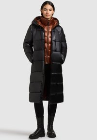 Fekete pufferkabát kapucnival, fényes felülettel, vízszintes steppelt mintával és kontrasztos barna belső réteggel. Cipzáras részletekkel kiemelve.