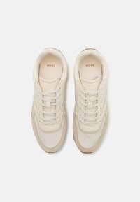 Beige tennarit, joissa on teksturoitu kankainen päällinen, nahkasuojukset ja luonnonvalkoiset nauhat. Hieman kohotettu "BOSS" -logo kengän kielessä.