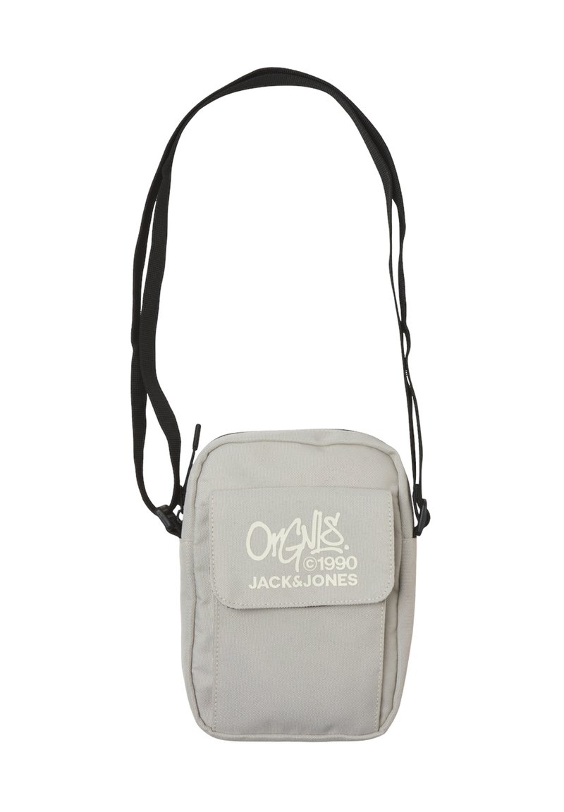 Bolso cruzado de tela gris con solapa frontal y acentos de logo blanco. Presenta una larga correa ajustable negra y forma rectangular.