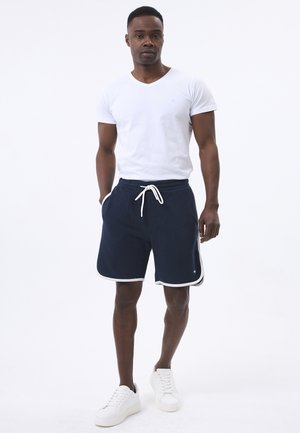 Navyblauwe sportshorts met witte zijstrip en trekkoord in de taille, gecombineerd met een eenvoudige witte V-hals t-shirt en witte sneakers.