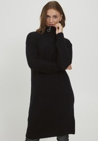 Abito in maglia nero con colletto alto e mezza zip. Presenta una vestibilità comoda e una texture a coste che si estende fino al ginocchio.