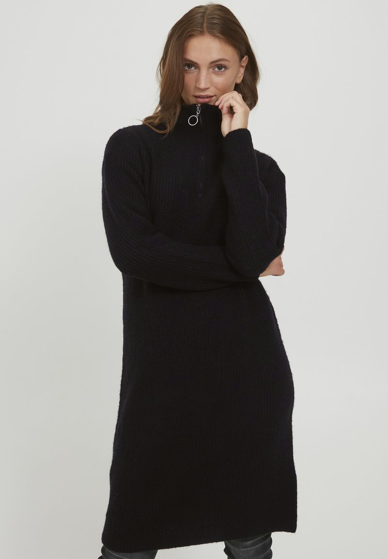 Abito in maglia nero con colletto alto e mezza zip. Presenta una vestibilità comoda e una texture a coste che si estende fino al ginocchio.
