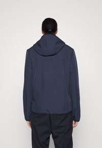 Marinblå softshelljacka med huva, med en slät yta och elastiska ärmslut, designad för en åtsittande siluett.