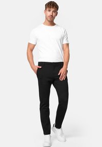 Pantalones negros ajustados con una textura suave y corte slim, combinados con una camiseta blanca de manga corta y zapatillas blancas.