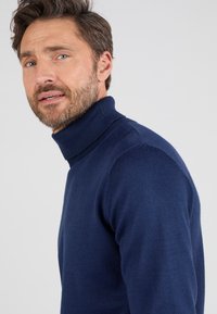 Suéter de cuello alto azul marino hecho de un tejido suave, con un diseño ajustado y cuello de canalé. Mangas ceñidas y líneas limpias.