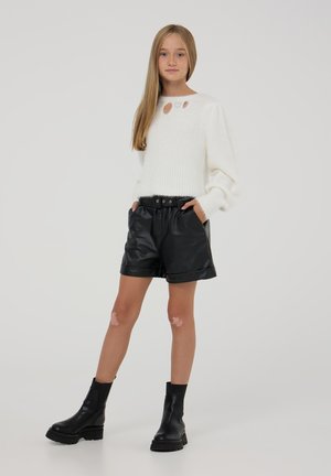Biały sweter robiony na drutach z okrągłym dekoltem i trzema dużymi dziurami. Czarne szorty z sztucznej skóry z elastycznym pasem i kieszeniami. Czarne botki sięgające kostek.