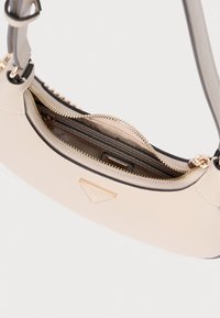 Jasnobeżowa torebka o gładkiej fakturze, zaokrąglonym kształcie i złotym logo. Posiada przegródkę na zamek oraz kilka miejsc na karty.