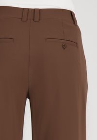Bruine broeken met een gladde textuur, voorzien van twee achterzakken, een enkele knoopdetail en riemlussen in de taille.