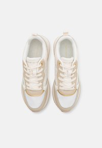 Zapatillas beige y blancas con parte superior de malla y cuero, cordones gruesos y una puntera con acentos dorados. Presenta detalles texturizados en los laterales.