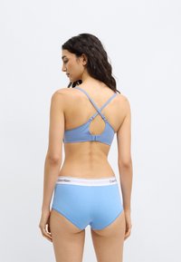 Modrý bralet s dizajnom na chrbte typu racerback a nastaviteľnými ramienkami, v páre so svetlomodrými hipster nohavičkami s bielym pásom.