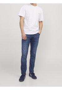 Vit bomull t-shirt med kort ärm, blå denimjeans och marinblå sneakers med vita detaljer. Avslappnad outfit, åtsittande design.