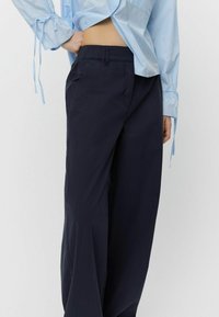 Marineblaue, lockere Hose mit elastischem Bund und seitlichen Taschen; aus leichtem Stoff mit glatter Textur gefertigt.