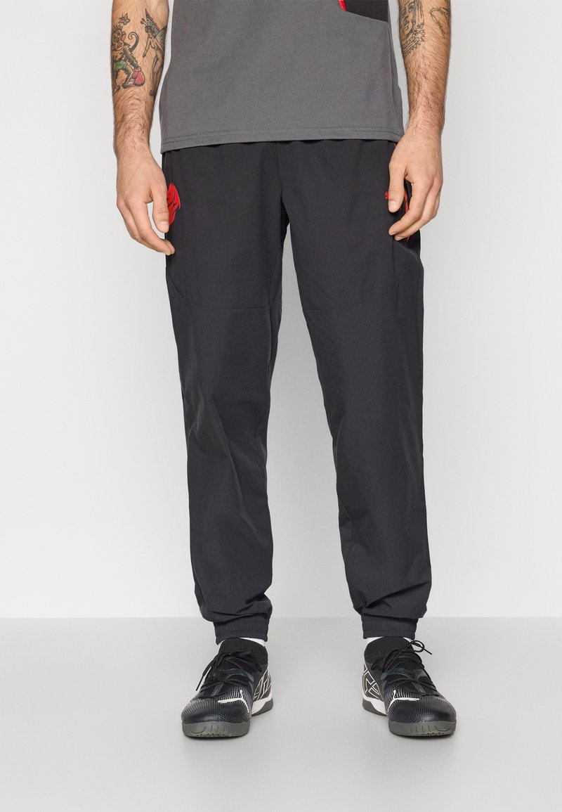 Sorte træningsbukser med elastisk waistband og smalle ankler, forsynet med et rødt logo på venstre lomme og lavet af et glat, let materiale.