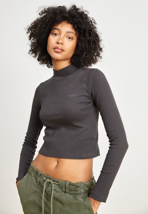 Hallmarked halliga pikkade varrukatega kõrge kaelusega tipp, millel on lühendatud disain ja tagasihoidlik logodetail rinnal, koos oliivroheliste nöörpükstega.