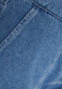 Světlá modrá džínovina s měkkou strukturou, která má jemný lesk, šikmé švy a viditelné detaily stehů.