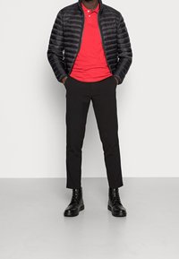 Musta puffatakki vaakasuorilla viivoilla, punainen poolopaita, slim-fit mustat housut ja mustat nauhakengät. Minimalistinen muotoilu, tasaiset värit.