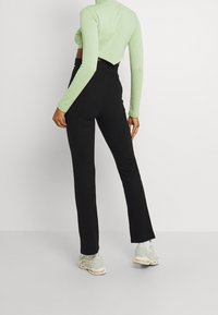 Svarta, ribbade, utsvängda byxor matchade med en ljusgrön, ribbad, långärmad crop top. Skorna är ljusgrå sneakers med accenter.