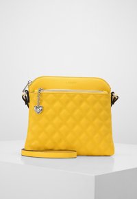 Keltainen nahkainen käsilaukku, jossa on tikattu kuvio, hopeiset yksityiskohdat, sydämen muotoinen riipus ja säädettävä olkahihna. Vetoketjukiinnitys päällä.