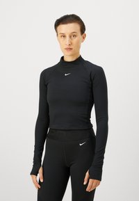 Schwarzes langärmliges Sportoberteil mit einem Stehkragen, glatter Textur und einem kleinen weißen Logo auf der Brust. Kombiniert mit schwarzen Leggings.