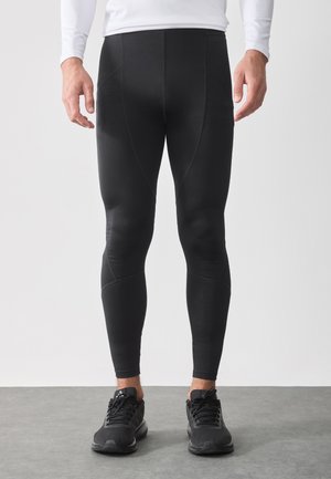 Black athletic leggings with a fitted design, featuring smooth texture and panel accents. Worn with black running shoes on a grey surface.