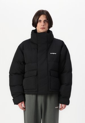 Melnā pūkainā jakā ar augstu apkakli un divām priekšējām kabatām. Iezīmējas ar izšūtiem paneļiem un logotipu kreisajā krūtī. Gluda tekstūra.