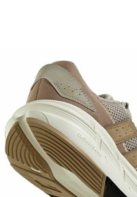 Scarpa da corsa leggera con tomaia in mesh beige con accenti grigi, intersuola bianca ammortizzata e suola in gomma texturizzata.