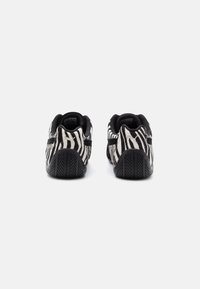 Black and white zebra-patterned sneakers with a textured upper, flat sole, and a black rubber tread. Dual-tone design accentuates the pattern.