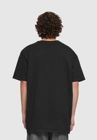 Crna oversized majica od pamuka, s okruglim izrezom i kratkim rukavima, prikazana s leđa s jednostavnim dizajnom.