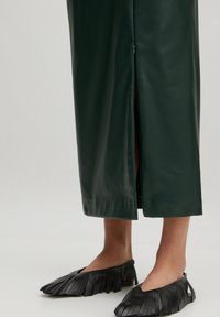 Grüne Leder-Maxi-Rock mit einem seitlichen Schlitz, kombiniert mit schwarzen Fransen-Ballerinas mit offener Silhouette und weichem Material.