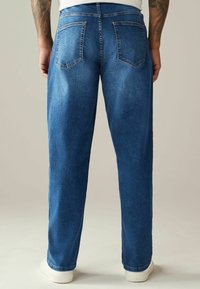 Jeans din denim albastru, cu croi drept, dotate cu două buzunare pe spate, detalii de vechire și cusături albe. Finalizate cu margini rulate și purtate cu teniși albi.