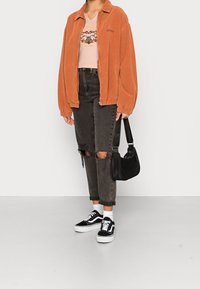 Oranžová kordovou zipovou bundou, bledě růžovým tričkem s potiskem, roztrhanými černými džíny a černými nízkými teniskami s bílými akcenty, doplněnými černou kabelkou.