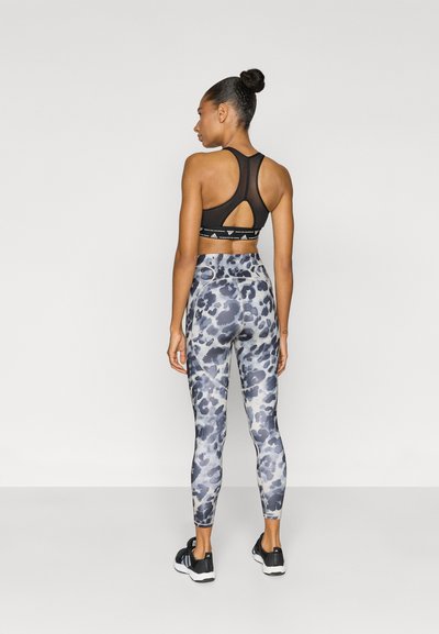 Black sports bra with a cutout back and patterned gray leggings featuring a leopard print, paired with black athletic shoes.