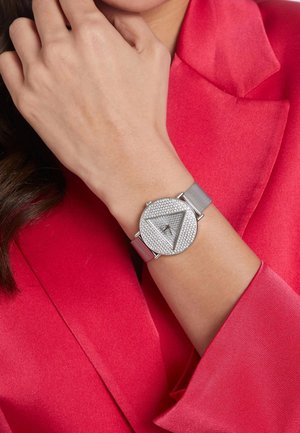 Reloj de malla plateada con una cara triangular adornada con rhinestones. El reloj presenta marcadores de hora mínimos y un diseño elegante.