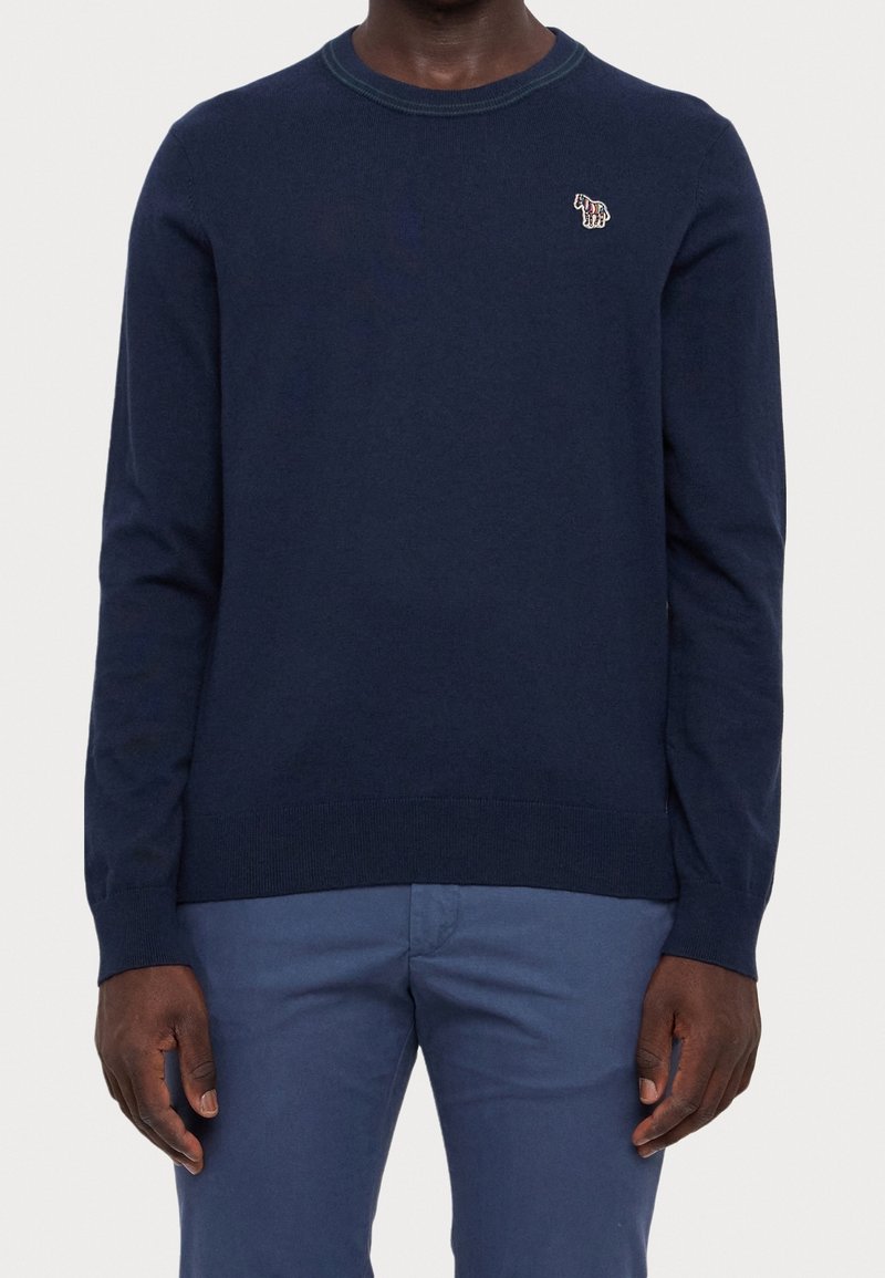 Mörkblå stickad tröja med långa ärmar och rundad halsringning. Har en subtil broderad design på bröstet samt ribbade detaljer vid fållen och ärmsluten.