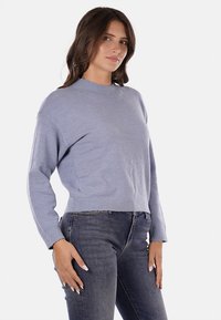 Maglioncino azzurro chiaro a maniche lunghe, realizzato in tessuto morbido, con scollatura rotonda, abbinato a jeans in denim scuro.