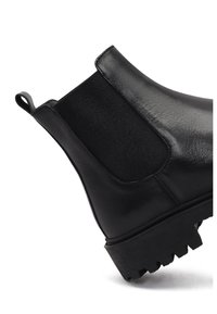 Bottines Chelsea en cuir noir avec panneaux élastiques sur les côtés, semelle en caoutchouc texturée et languette de traction. Équipées d'une finition lisse et d'un design à bout arrondi.