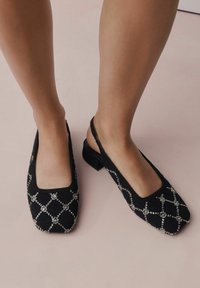 Sorte slingback flade sko med firkantede tæer, tekstureret stof og sølvfarvet perlediamantmønster. Lav blokhælm giver stabilitet.