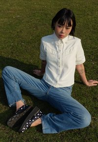 Hvit kortermet skjorte med knapper og klaffelomme, sammen med blå jeans og marineblå platå-sko prydet med hvite prikker.