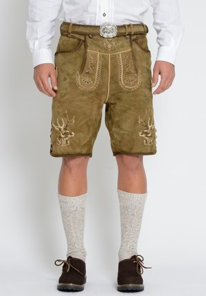 Mężczyzna noszący tradycyjne brązowe skórzane lederhosen z haftowanymi głowami jeleni, białą koszulę, wełniane skarpety do kolan i ciemnobrązowe buty.